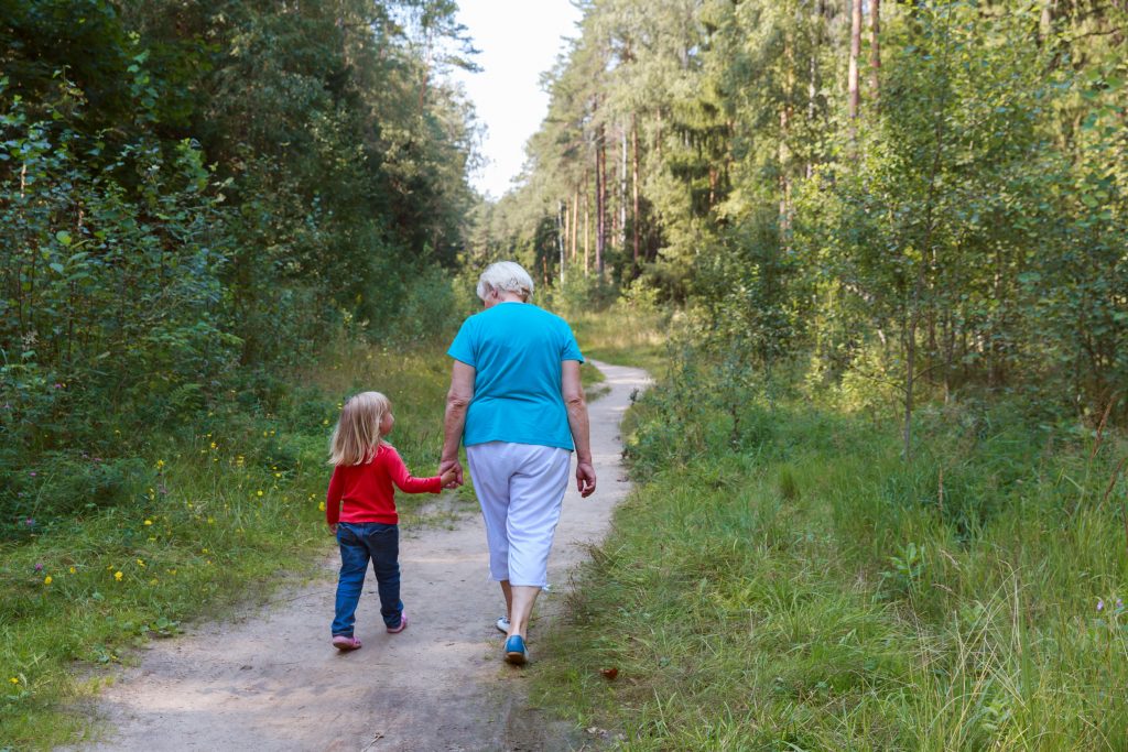 Grandmother walking with grandchild along a forest path.